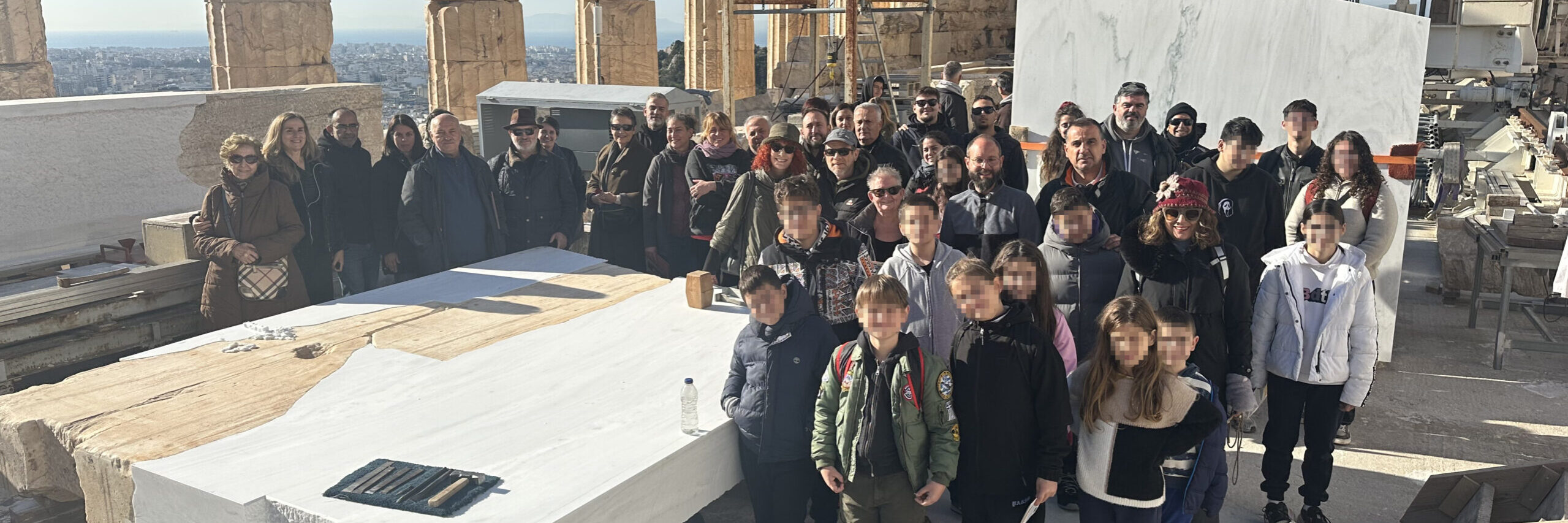 Οικογένειες εργαζομένων στο εσωτερικό του Παρθενώνα ποζάρουν γύρω από ένα λίθο ορθοστάτη τυμπάνου από το δυτικό αέτωμα. Σε πρώτο πλάνο παιδιά ηλικίας 6 έως 15 ετών.