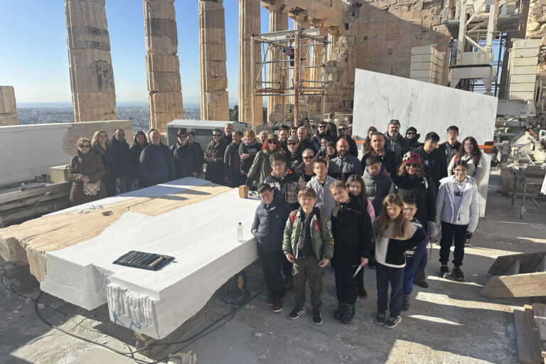 Οικογένειες εργαζομένων στο εσωτερικό του Παρθενώνα ποζάρουν γύρω από ένα λίθο ορθοστάτη τυμπάνου από το δυτικό αέτωμα. Σε πρώτο πλάνο παιδιά ηλικίας 6 έως 15 ετών.