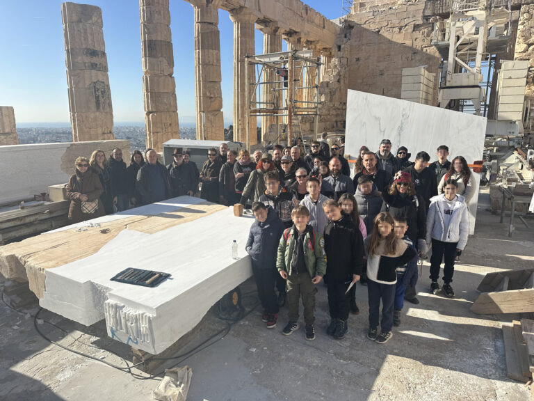 Οικογένειες εργαζομένων στο εσωτερικό του Παρθενώνα ποζάρουν γύρω από ένα λίθο ορθοστάτη τυμπάνου από το δυτικό αέτωμα. Σε πρώτο πλάνο παιδιά ηλικίας 6 έως 15 ετών.